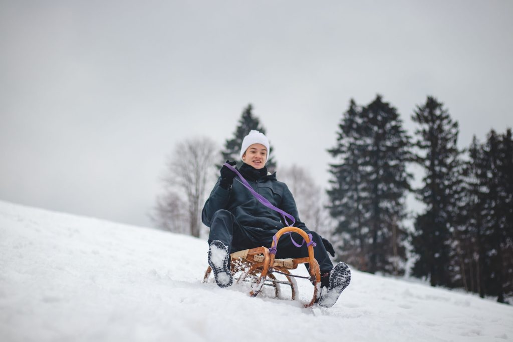 Joyful Smile Of A Young Sixteen Year Old Boy Riding A Historic Wooden Sled On A Ski Slope. Dangerous Driving. Enjoying The Fallen Snow In Winter. Fooling Around At A Young Age. Immortality.